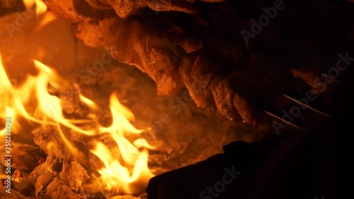 Skewered meat sizzles as it is grilled over crackling flames in a fireplace. Traditional Mtsvadi preparation over an open fire at night, close-up view. photo