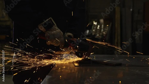 Closeup scene of unrecognisable person using emery to cut metal. Dark scene of hands working on metal photo