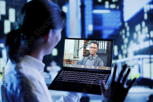 Asian man in videocall with coworker while strolling around city streets at night, giving him work updates. Person using laptop to show colleague surroundings in nighttime urban environment