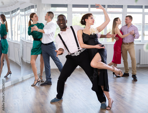 Dynamic middle-aged male and female attendees of dancing courses doing waltz in group