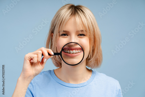 Smiling young beautiful woman holding magnifying glass showing teeth with braces looking at camera photo