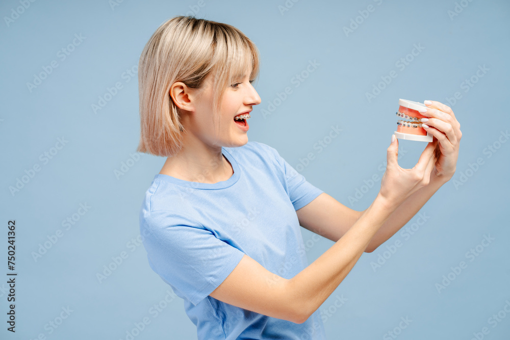 Beautiful, smiling young woman with blond hair with braces holding jaw and looking away Beautiful, smiling young woman with blond hair with braces holding jaw and looking away