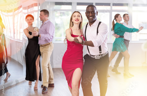 With unhurried music, woman with African man in couple spins to rhythm of waltz during lesson for novice students. Classes in mini-groups for those who want to learn dancing