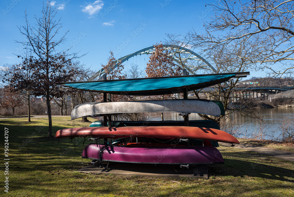 Colorful canoes with Birmingham Bridge across the Allegheny River and a blue sky seen from Three Rivers Heritage Trail, Pittsburgh, on an early sunny spring day. Colorful canoes with Birmingham Bridge across the Allegheny River and a blue sky seen from Three Rivers Heritage Trail, Pittsburgh, on an early sunny spring day.
