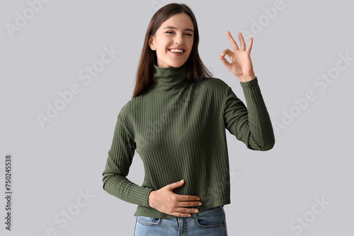 Young woman with healthy stomach showing OK on light background