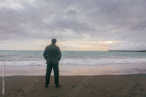 Solitary man standing by the seaside and staring in the distance. He's wearing a military outfit and is not recognizable.