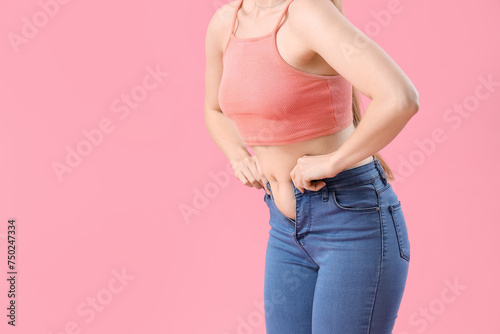 Young woman in tight jeans on pink background, closeup. Weight gain concept © Pixel-Shot