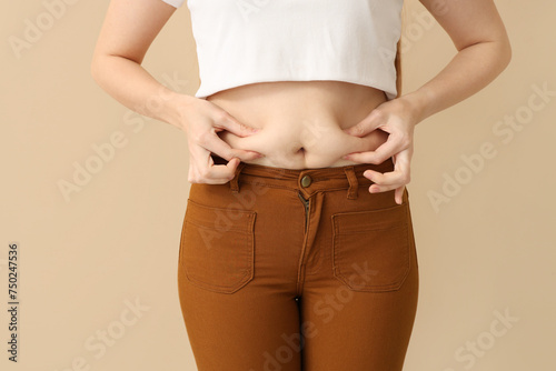 Young woman in tight pants on beige background, closeup. Weight gain concept
