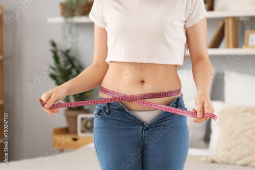 Young woman in tight jeans measuring her belly at home, closeup. Weight gain concept © Pixel-Shot