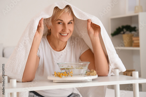 Mature woman with towel doing steam inhalation in bedroom photo