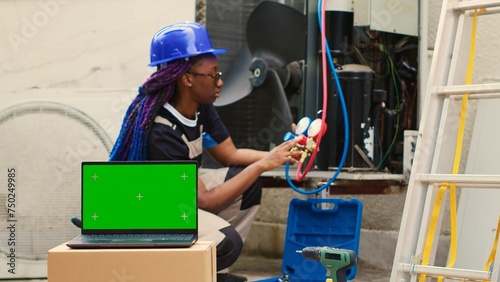 Capable specialist contracted by home owner to detect HVAC system problems, checking real-time superheat and subcooling values measured by manifold gauges displayed on green screen laptop photo