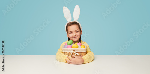 Adorable girl in bunny ears sitting with basket of eggs
