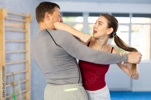 Aggressive young girl practicing self-defense techniques in pair with middle-aged man during workout session