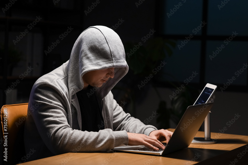 Hacker using laptop at table in dark room Hacker using laptop at table in dark room
