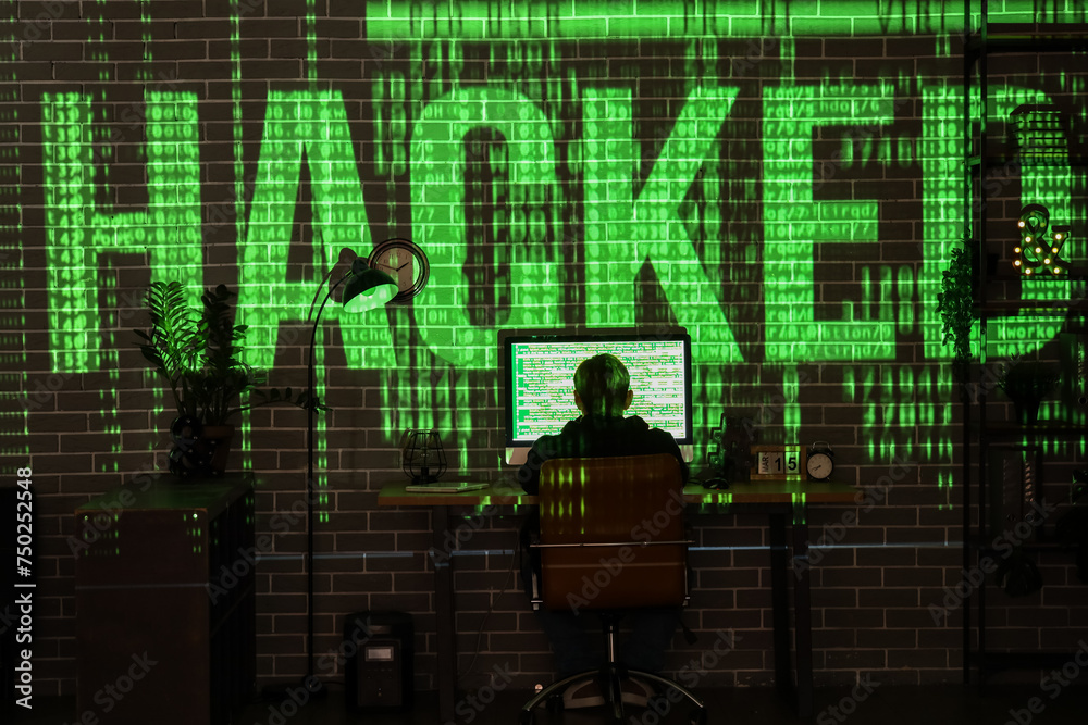 Obraz premium Hacker using computer at table and projection of word HACKED in dark room