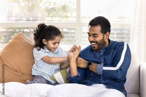 Positive young Indian dad playing fight with active little daughter kid, tickling, cuddling child, smiling, laughing, enjoying family leisure, playtime at ohme, fatherhood, closeness