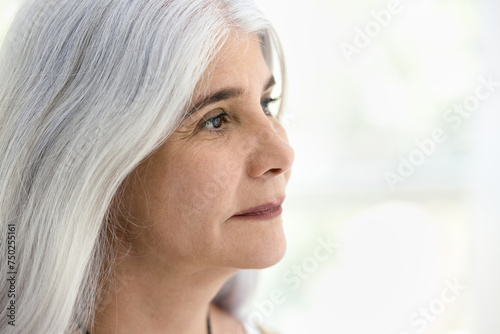 Face of calm positive old retired woman with natural make up and long grey haired looking at copy space away, thinking on elderly beauty care, skincare, dreaming. Close up casual portrait © fizkes
