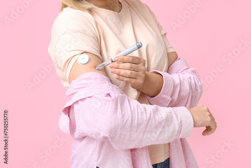 Woman with glucose sensor for measuring blood sugar level and lancet pen on pink background. Diabetes concept