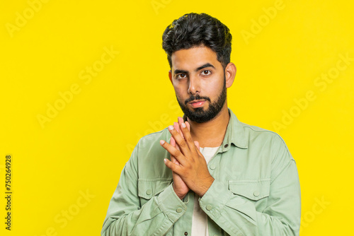 Sneaky cunning Indian young man with tricky face gesticulating and scheming evil plan, thinking over devious villain idea, cheats, jokes, pranks. Arabian Hindu guy isolated on yellow studio background