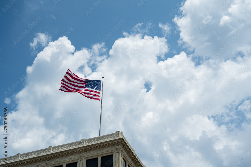 Fototapeta premium United States Flag flying on top of building with blue sky and white clouds