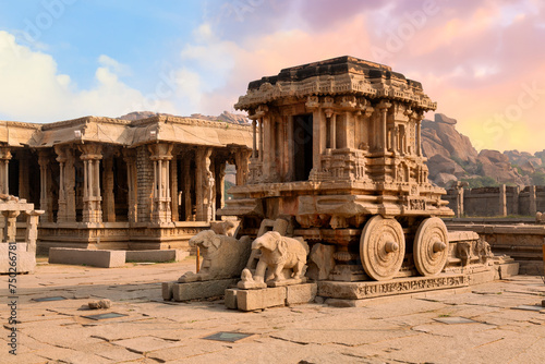 Famous ancient stone chariot of Hampi in closeup view with other architecture ruins at Karnataka, India, at sunset. 