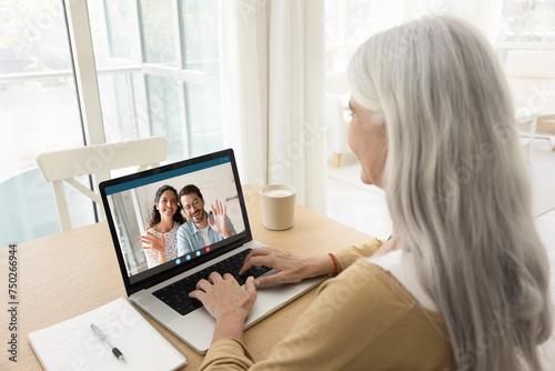 Happy young married couple talking to senior mom on video call, waving hands from laptop screen, smiling, enjoying online family meeting, distant Internet communication