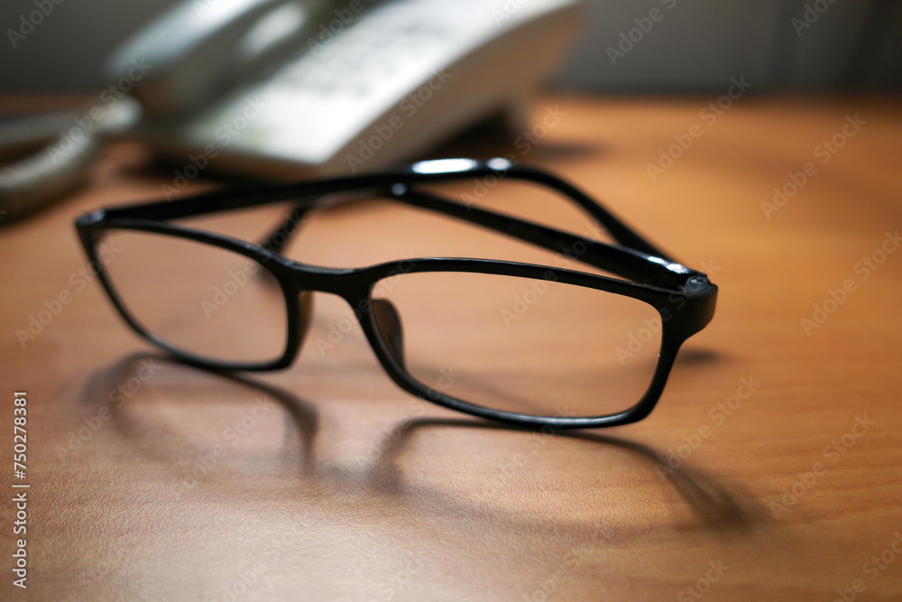 A black eyeglasses and an old landline telephone on wood table, shallow focus A black eyeglasses and an old landline telephone on wood table, shallow focus