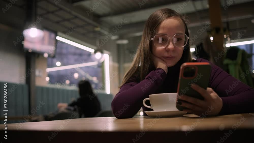 A woman comfortably sits in a warmly lit coffee shop during evening hours, sipping on fresh coffee and scroll the smartphone screen, possibly browsing the internet or checking messages. A woman comfortably sits in a warmly lit coffee shop during evening hours, sipping on fresh coffee and scroll the smartphone screen, possibly browsing the internet or checking messages.