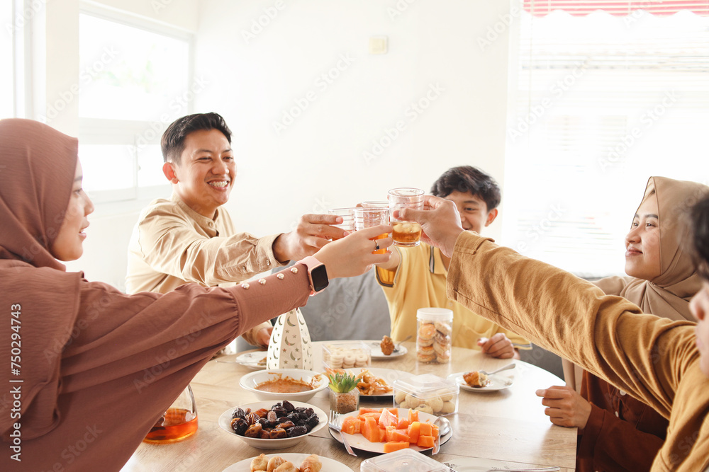 Laughing muslim family and friends toasting with tea while sitting around a table when breakfasting together at home