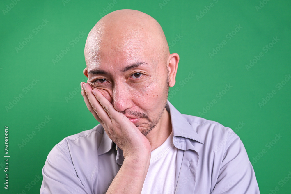 Bald man looking tired and bored with depression problems against green background Bald man looking tired and bored with depression problems against green background