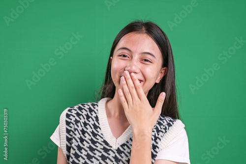 Portrait of happy Asian young woman laughing and covering her mouth over green background.