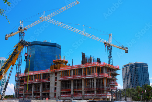City first-stage building construction showing blocks, concrete and steel makings of the structure with large cranes on a sunny blue sky morning.