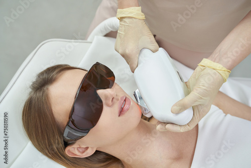 Laser facial treatment for hair removal and rejuvenation at spa. White equipment enhances beauty and skin care. The cosmetologist uses advanced technology for therapy, promoting health, cosmetic care photo