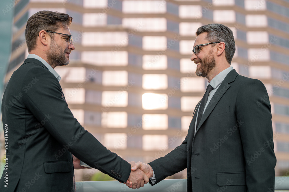 Two businessmen shaking hands on city street. Business men in suit shaking hands outdoors. Handshake between two businessmen. Handshake with partner in the city for greeting, dealing, merger. Two businessmen shaking hands on city street. Business men in suit shaking hands outdoors. Handshake between two businessmen. Handshake with partner in the city for greeting, dealing, merger.