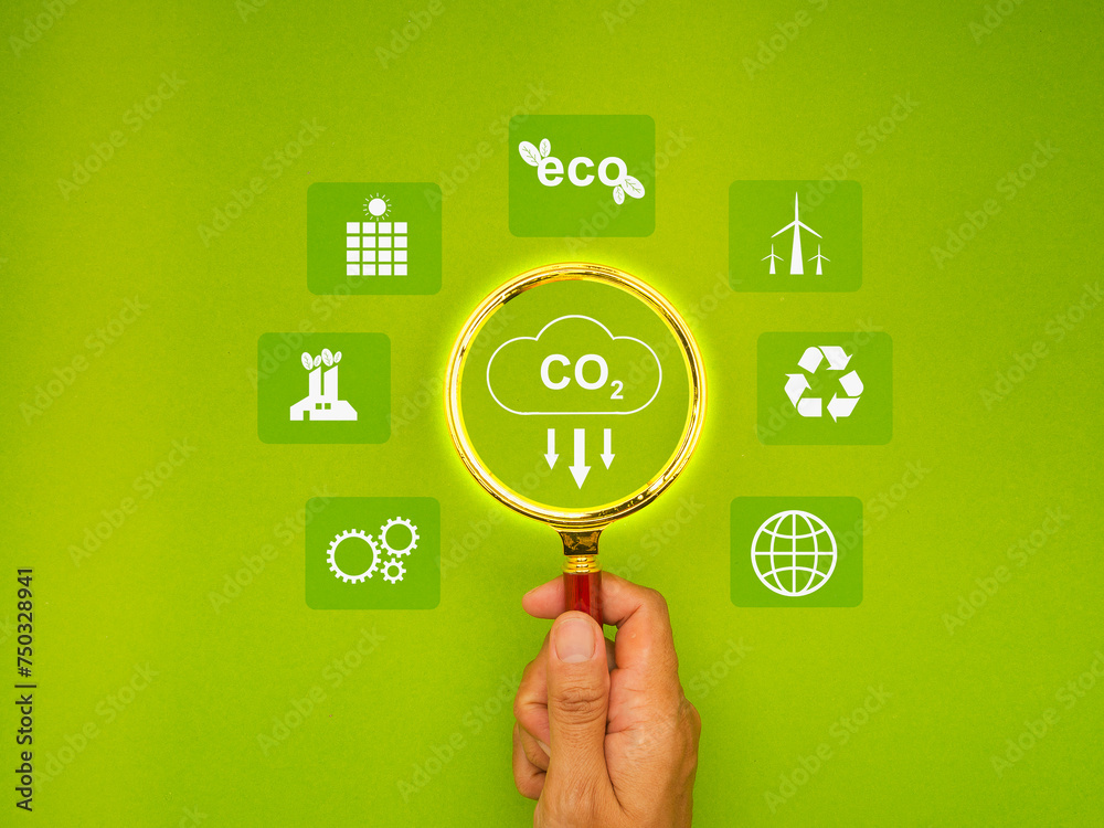Hand holding a magnifying glass with a CO2 icon over a green background. Hand holding a magnifying glass with a CO2 icon over a green background.