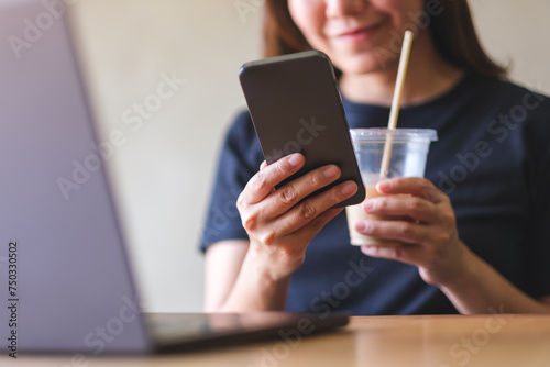 Closeup image of a young woman drinking coffee, chatting on mobile phone while using laptop computer