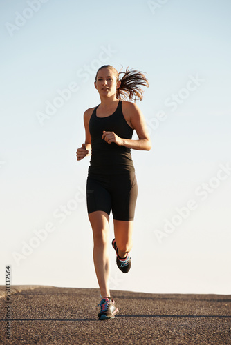 Woman, running in street and exercise for cardio, health and fresh air when training for marathon with sky background. Sports, exercise and athlete in city for workout, wellness and endurance outdoor