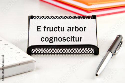 E fructu arbor cognoscitur the phrase in Latin translates as the Tree is known by its fruits on a white business card next to a calculator, notepad and pen photo
