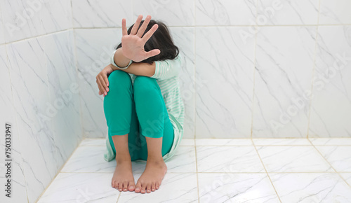Unhappy depressed asian child sitting on floor at home. Holding out hand indicates resistance. Concept for campaign against child violence, abuse, pain, and bullying. 