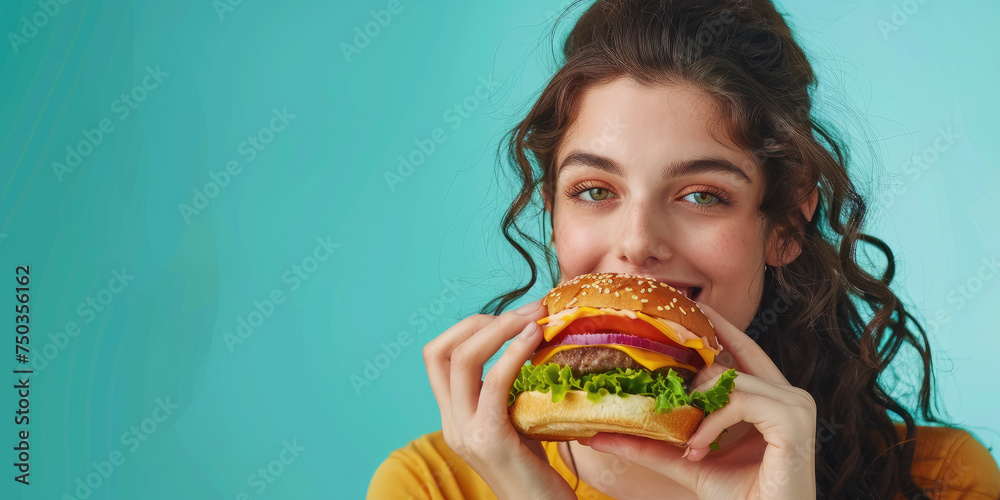 portrait of a young woman eating delicious hamburger on color background, copy space