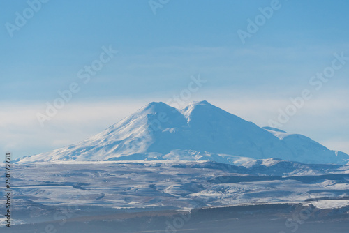 View from the road of the snow-covered majestic double-headed Elbrus in the morning haze. Close-up. Elbrus is the main attraction of Kabardino-Balkaria. December 2023