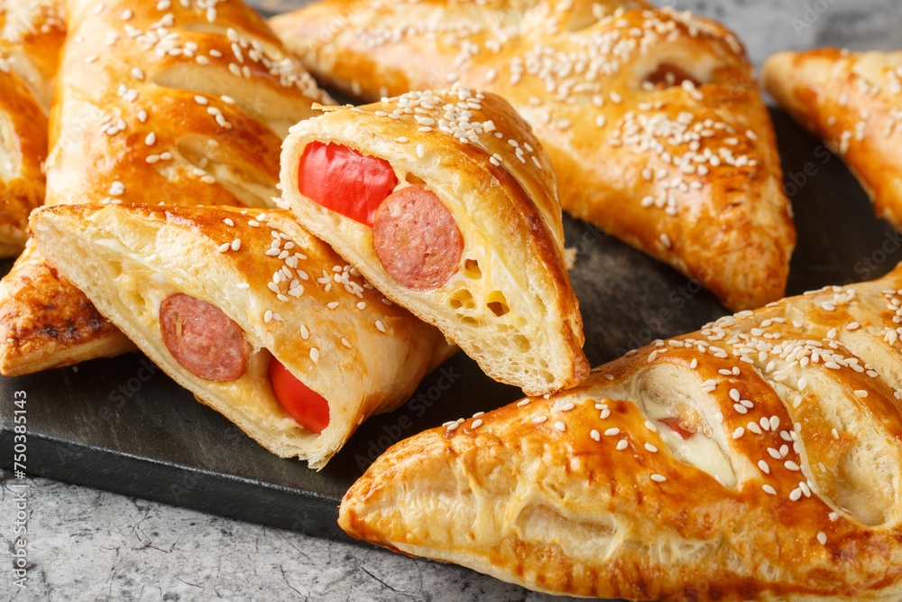 Pigs in blankets puff pastry turnover with sausage, cheese and pepper close-up on a marble board on the table. Horizontal