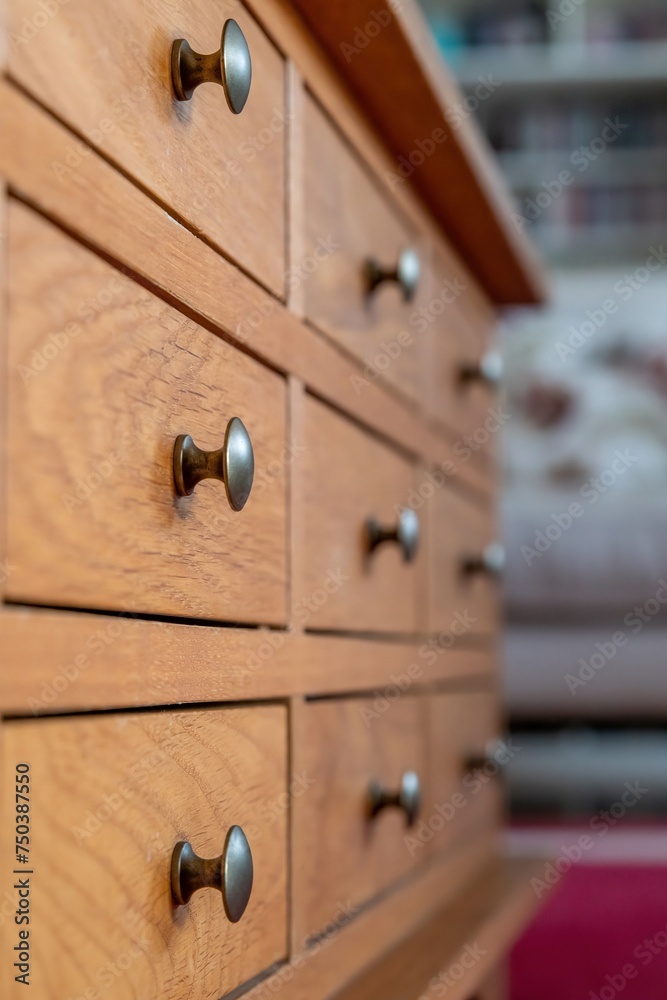 Wooden cabinet of small drawers in a lounge setting with metal pull knobs. Stylish traditional home storage furniture. Home living interiors design. Focus in the foreground. Wooden cabinet of small drawers in a lounge setting with metal pull knobs. Stylish traditional home storage furniture. Home living interiors design. Focus in the foreground.