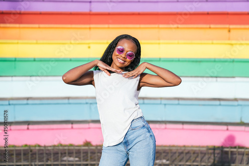 Happy afro woman with stylish shades over a rainbow-colored LGBT wall