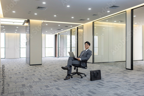 Confident businessman using laptop in empty office photo