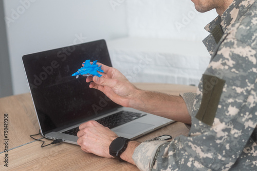 Military Technical Service, Air Force Concept. Hands of a man in uniform holding a silver toy airplane. A middle-aged adult man in a green camouflage uniform. Indoors. 