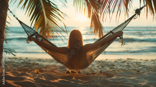 A woman is captured from behind as she rests in a hammock on the beach, surrounded by palm trees, gazing directly at the ocean illuminated by the golden rays of sunset.