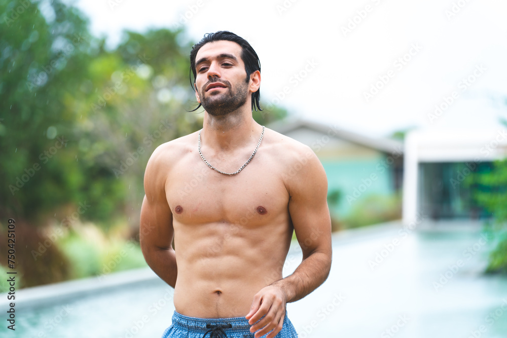Fototapeta premium Feel the sun and music by the pool. A handsome man is refreshing in the pool water and listening to his favorite song. Swimming and sunbathing, hot summer day and enjoying summer days and rest