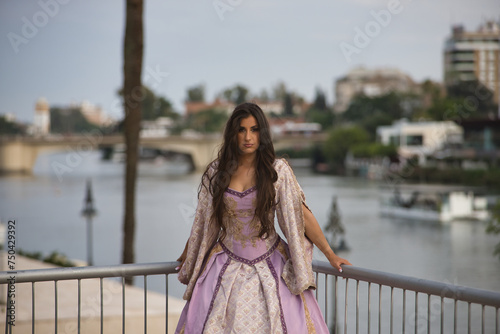 Young woman, Hispanic, beautiful, brunette, in elegant vintage violet dress , posing leaning on a railing while visiting the city. Concept of beauty, fashion, trend, elegance, antique.
