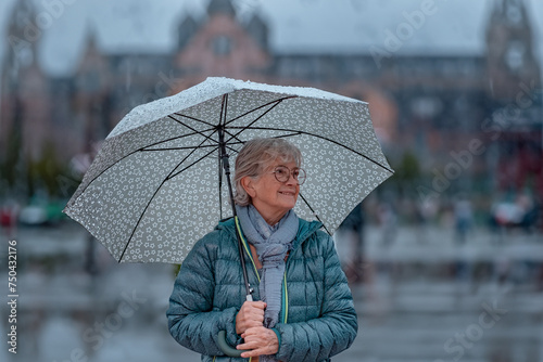 Senior woman walking in the city in a rainy day holding an umbrella while strolling outside. Copy space